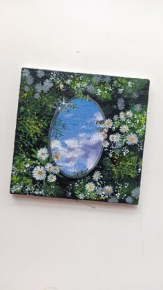 there is a mirror on the wall with daisies in front of it and clouds in the background