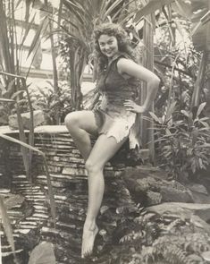 an old black and white photo of a woman sitting on a ledge in the jungle
