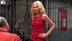 a woman in a red dress standing next to a man in a jail cell area