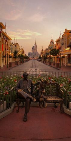 a statue sitting on top of a bench in front of a street filled with flowers