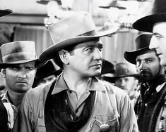black and white photograph of three men in hats looking off to the side with other men standing behind them