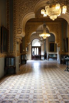 an ornate hallway with chandeliers and paintings on the walls, leading to another room