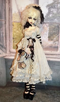 a doll is standing in front of a window wearing a white dress and black shoes