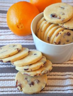 a bowl filled with cookies next to oranges on a striped table cloth and another bowl full of cookies in the background