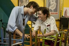 two people sitting in chairs and one is touching the other's face