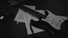 a black and white photo of an electric guitar laying on top of music sheet paper