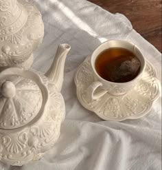 a tea pot and saucer sitting on top of a white cloth covered tablecloth