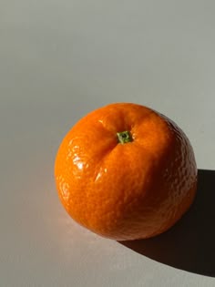 an orange sitting on top of a white table next to a shadow from the sun