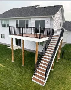 a deck with stairs and railings in front of a white house on green grass