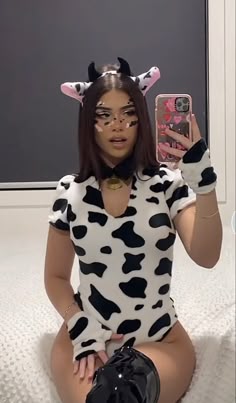 a woman in a cow costume is taking a selfie with her cell phone while sitting on the floor
