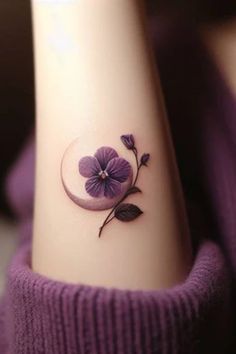 a small purple flower tattoo on the left side of the arm, with green leaves