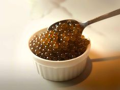 a spoon full of brown sugar on top of a white bowl filled with orange beads