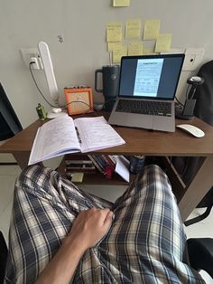 a person is sitting at a desk with an open book and laptop on his lap