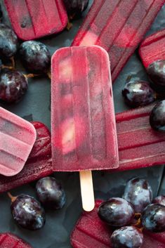 an ice lolly popsicle sitting on top of purple grapes next to other fruit