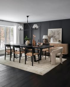 a dining room with black walls and wooden flooring is pictured in this image, there are several chairs around the table