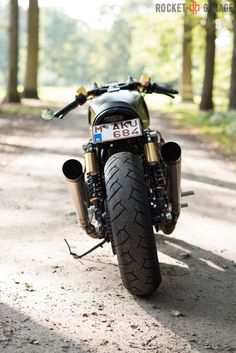 a motorcycle parked on the side of a dirt road in front of trees and grass