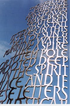 a tall metal sculpture with many different letters on it's sides and the sky in the background