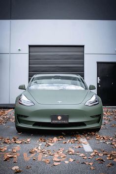 a green sports car parked in front of a garage door with leaves on the ground