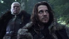 the two men are standing together in the woods, one is wearing a fur coat