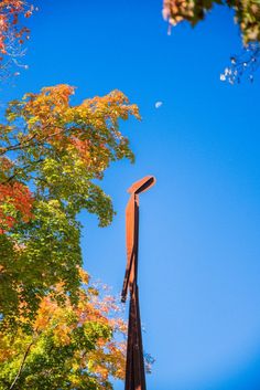 a tall metal sculpture sitting next to a forest filled with trees in the fall time