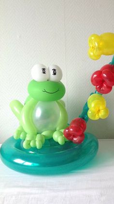 a frog figurine sitting on top of a blue base with balloons attached to it