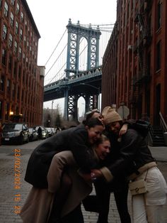 four people are hugging in front of the brooklyn bridge