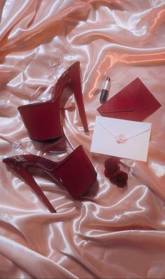 a pair of red high heeled shoes next to a note and pen on a satin surface
