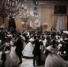 a group of people dressed in formal clothing dancing together with chandeliers hanging from the ceiling