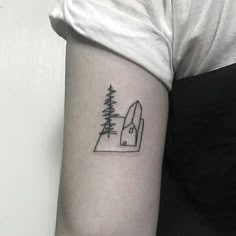 a woman's arm with a small tattoo of trees and a house on it