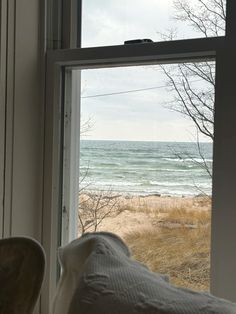 an open window looking out onto the beach and ocean from inside a room with a chair