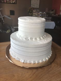 a three tiered white cake sitting on top of a wooden table next to a plate