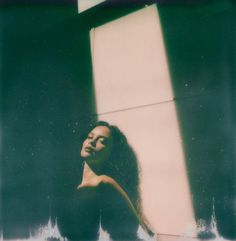 a woman standing in front of a window with her hair blowing back and looking up