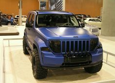 a blue jeep is on display in a showroom with other cars and motorcycles behind it