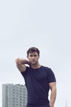 a man standing in front of a tall building with his hand on his head and looking at the camera