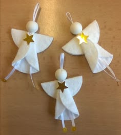 three white angel ornaments with gold stars hanging from strings on a wooden table, ready to be made into christmas decorations