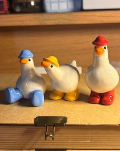 three ceramic ducks sitting next to each other on top of a wooden box in front of a bookshelf