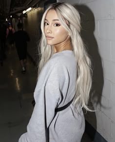 a woman with long white hair standing next to a wall and looking at the camera