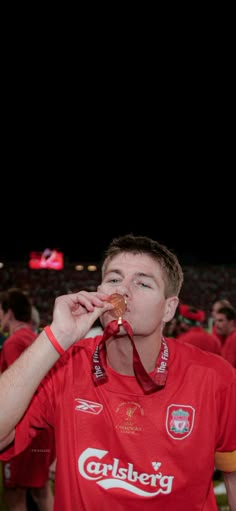 a young man in a red shirt is drinking from a bottle while standing on the field