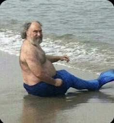 an older man sitting on the beach with his legs spread out and feet in the water