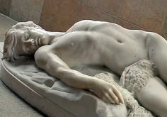 a statue of a man laying on top of a white bed next to a wall