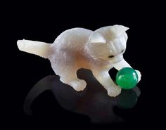 a white cat playing with a green ball on a black surface in front of a black background