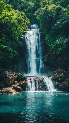 a large waterfall in the middle of a forest filled with green trees and rocks, surrounded by blue water