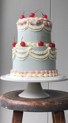 a three tiered cake with cherries on top is sitting on a wooden stool