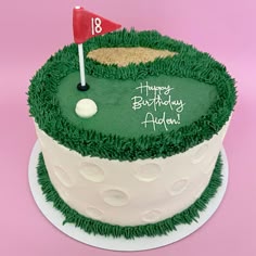 a birthday cake that is decorated with green grass and a golf ball on the top