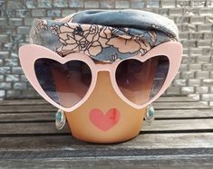 a hat with heart shaped sunglasses on top of it sitting on a wooden table next to a brick wall