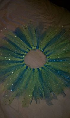a green and blue tulle with sparkles on it's side, sitting on a bed