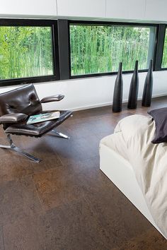 a modern bedroom with large windows and a leather chair in the foreground, next to a bed