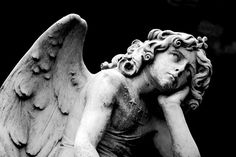 black and white photograph of an angel with its hands on his knees, looking down