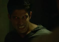 a man with red eyes and fangs on his face is looking at another man in the dark
