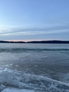 an icy lake with ice floes and trees in the distance